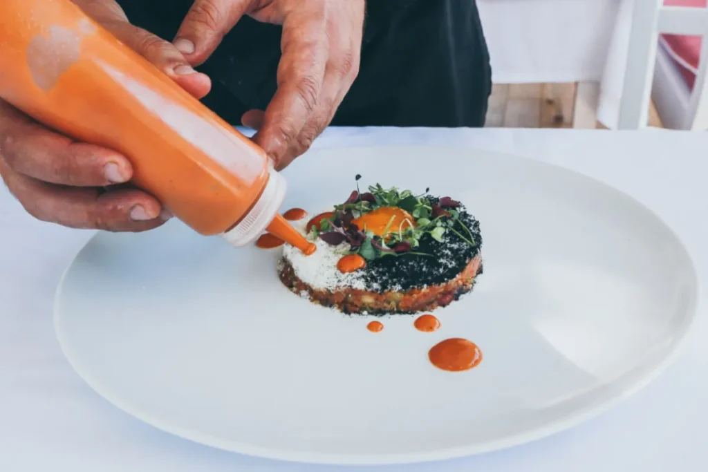Chef aplicando molho em prato sofisticado com apresentação artística em gastronomia molecular