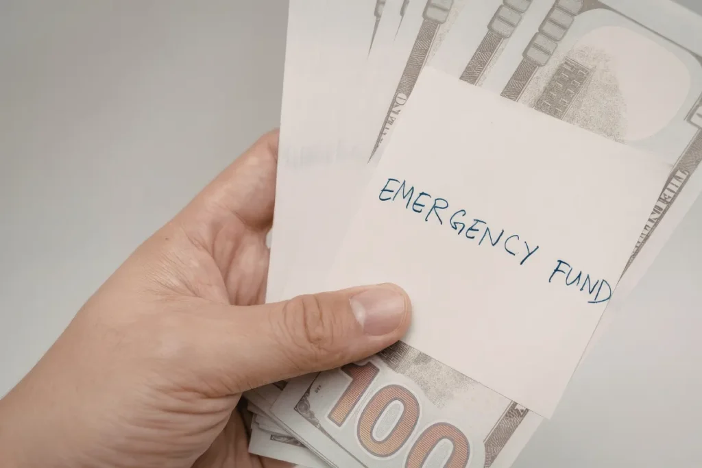 Mão segurando envelope escrito emergency fund com cédulas de dinheiro dentro