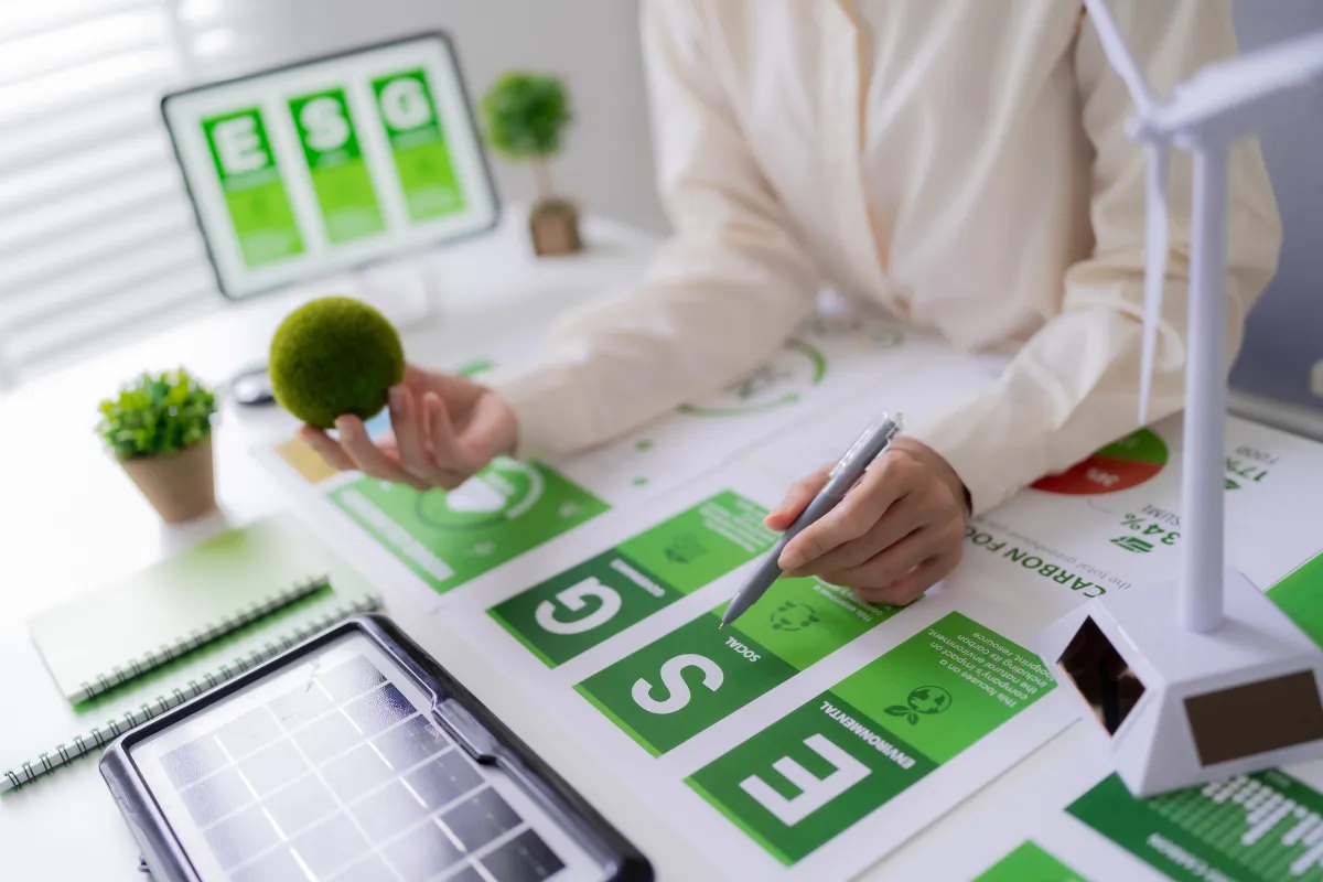 Profissional analisando materiais ESG com gráficos verdes e indicadores de sustentabilidade sobre mesa em ambiente corporativo
