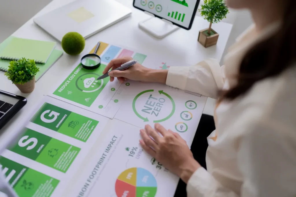 Pessoa analisando gráfico de redução de carbono e meta net zero com lupa e indicadores ESG em documentos sobre mesa