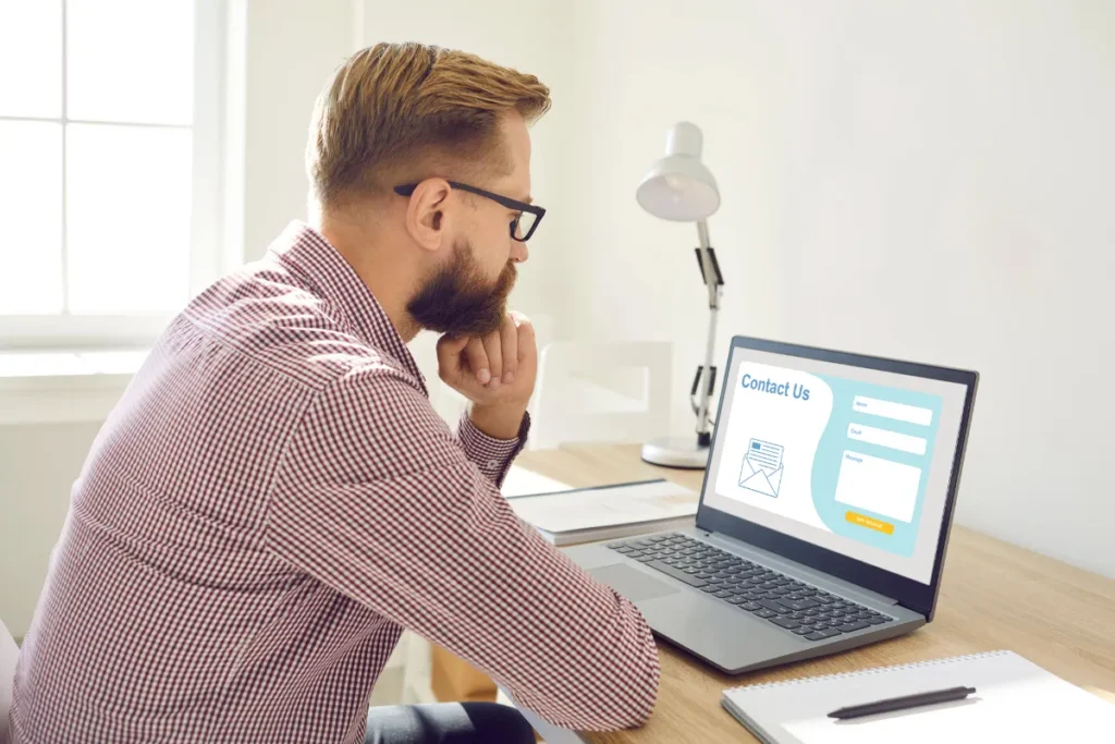 Homem observando landing page com formulário de contato em notebook, analisando experiência do usuário em ambiente de trabalho